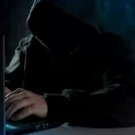 anonymous computer hacker in hoodie using laptop