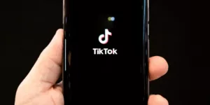 Hand of man holding a smartphone displaying the Tik Tok application logo